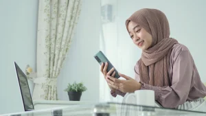 A woman using a mobile app at home, representing how technology in takaful insurance enables digital access, ease of use, and modern policy management.